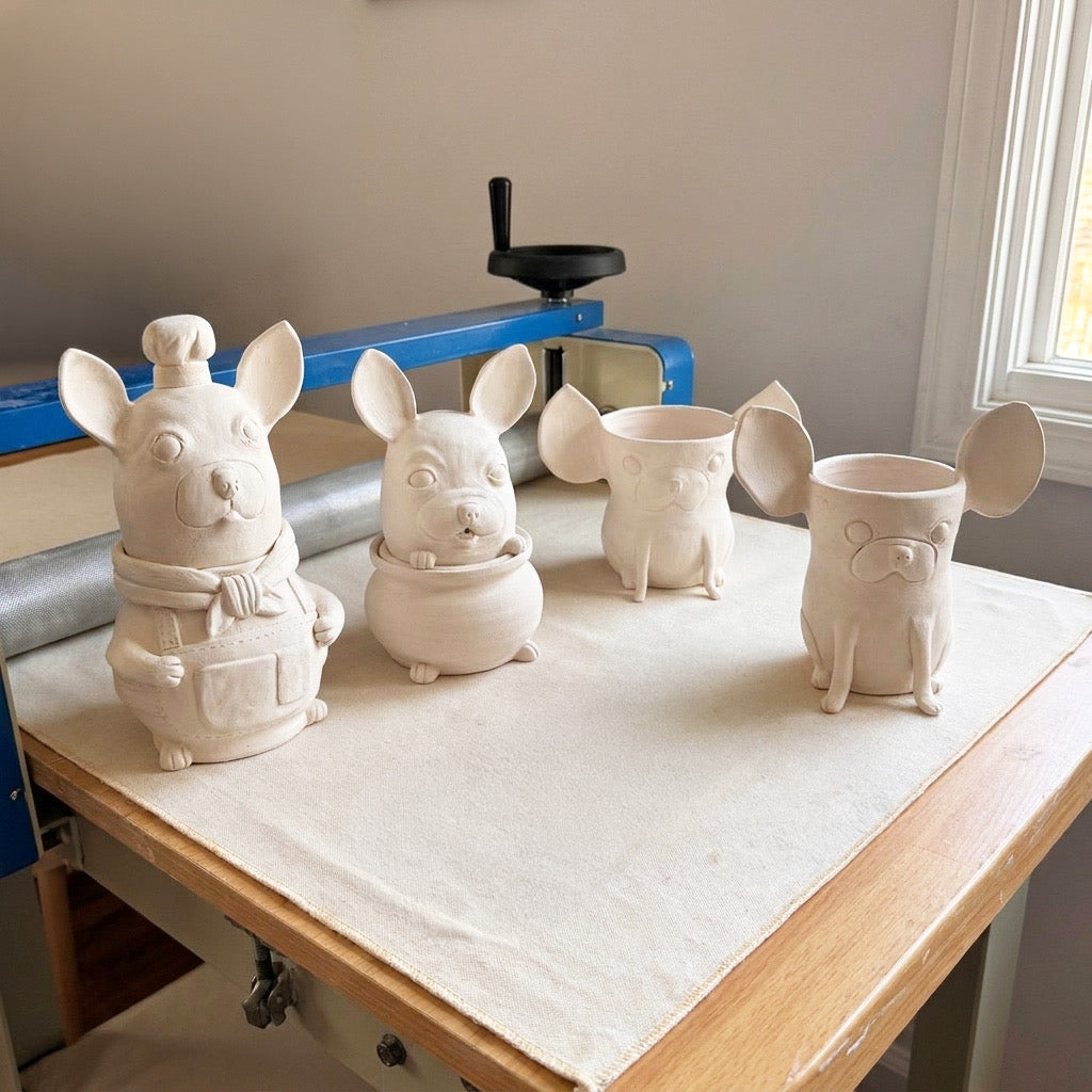 Lineup of unfired clay dog figurine mugs on the studio workbench